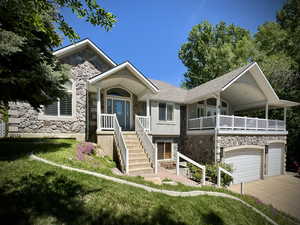 View of front facade featuring stone siding, driveway, roof with shingles, an attached garage, and a front lawn