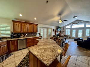 Kitchen with stainless steel dishwasher, a ceiling fan, open floor plan, vaulted ceiling, and backsplash