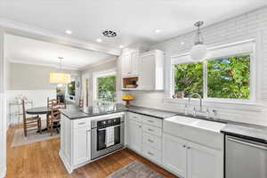 Kitchen featuring stainless steel appliances, a sink, a peninsula, white cabinets, and ornamental molding