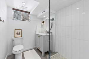 Bathroom featuring vanity, toilet, tiled shower, and baseboards