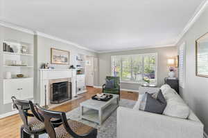 Living room featuring a fireplace, ornamental molding, wood finished floors, built in shelves, and baseboards