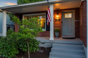 View of exterior entry with brick siding and a porch