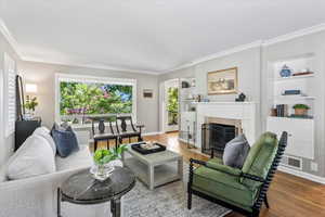Living area with built in shelves, crown molding, a fireplace, wood finished floors, and baseboards