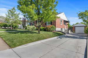 View of front facade with brick siding, driveway, a detached garage, an outdoor structure, and a front yard