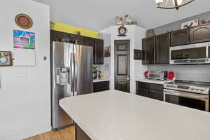 Kitchen featuring appliances with stainless steel finishes, light countertops, light wood finished floors, dark brown cabinets, and a chandelier