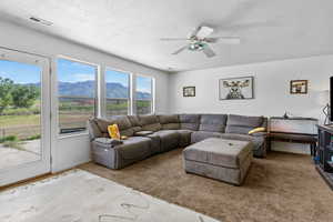 Living room featuring a mountain view, a textured ceiling, carpet floors, and a ceiling fan
