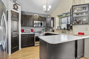 Kitchen featuring stainless steel appliances, a sink, light countertops, a peninsula, and vaulted ceiling