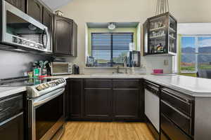 Kitchen featuring appliances with stainless steel finishes, a sink, light wood-type flooring, light countertops, and a peninsula
