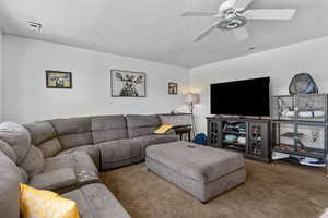 Living area with carpet, a ceiling fan, and a textured ceiling
