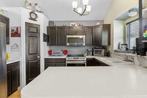 Kitchen featuring appliances with stainless steel finishes, a sink, light countertops, dark brown cabinets, and a peninsula