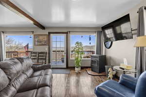 Living area featuring a wood stove, beam ceiling, wood-type flooring, and baseboards