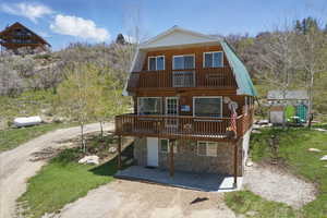 View of front facade with a balcony, a gambrel roof, stone siding, and a wooden deck