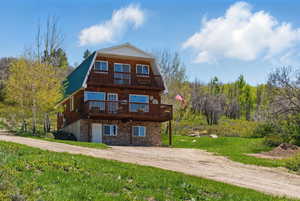 Back of house featuring a gambrel roof, stone siding, driveway, metal roof, and a deck