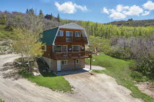 View of front of home featuring a gambrel roof, stone siding, a wooded view, dirt driveway, and metal roof