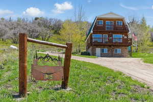 View of front of home featuring a balcony, a gambrel roof, stone siding, and driveway