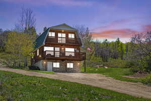 View of front of house with a gambrel roof, stone siding, metal roof, a wooden deck, and a front lawn