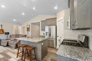 Kitchen with appliances with stainless steel finishes, a sink, open floor plan, light wood-style floors, and vaulted ceiling
