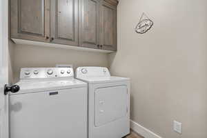 Laundry area featuring cabinet space, washer and dryer, baseboards, and wood finished floors