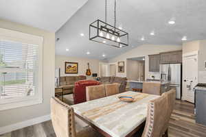 Dining space with dark wood-style floors, vaulted ceiling, and baseboards