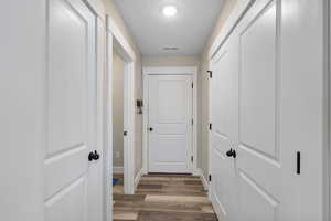 Hallway with a textured ceiling, wood finished floors, and baseboards
