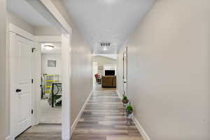 Hall with a textured ceiling, wood finished floors, and baseboards