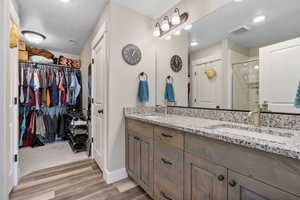 Bathroom with wood finished floors, a textured ceiling, double vanity, a stall shower, and a walk in closet