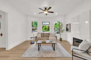 Living room featuring light wood-type flooring, a fireplace, baseboards, ceiling fan, and recessed lighting