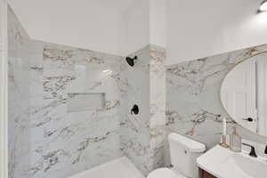 Bathroom featuring vanity, a marble finish shower, toilet, and tile walls