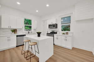 Kitchen featuring appliances with stainless steel finishes, backsplash, light wood finished floors, a kitchen bar, and recessed lighting