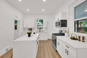 Kitchen with stainless steel appliances, a sink, tasteful backsplash, light wood-style floors, and white cabinetry