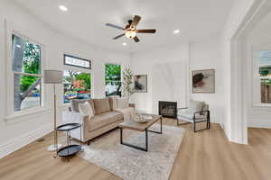 Living room featuring light wood finished floors, ceiling fan, recessed lighting, baseboards, and a fireplace