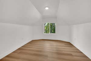 Bonus room with lofted ceiling, baseboards, and light wood-type flooring