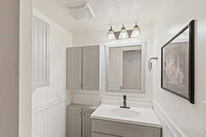 Bathroom featuring vanity, a textured ceiling, and wainscoting