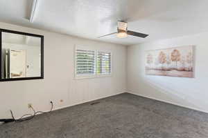 Carpeted spare room with a ceiling fan, baseboards, and a textured ceiling