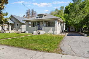 Bungalow-style house featuring covered porch, brick siding, a front lawn, and asphalt driveway