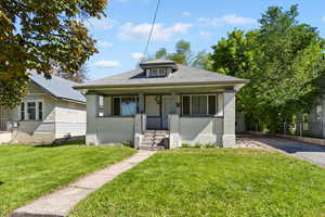 Bungalow-style home with brick siding, driveway, a front yard, and covered porch