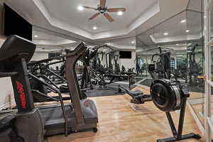 Gym featuring a ceiling fan, a raised ceiling, recessed lighting, and wood finished floors