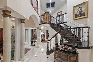 Tiled entrance foyer with decorative columns, a high ceiling, stairs, and arched walkways