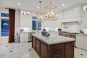 Kitchen with appliances with stainless steel finishes, a chandelier, a sink, a center island, and glass insert cabinets