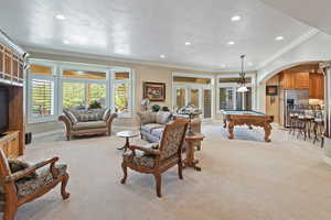 Living room featuring light colored carpet, arched walkways, billiards table, baseboards, and ornamental molding