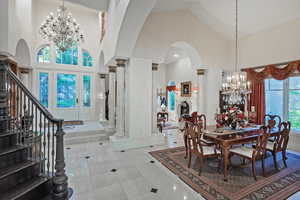 Dining room with high vaulted ceiling, a chandelier, arched walkways, ornate columns, and stairs