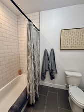 Bathroom with tile patterned floors, baseboards, shower / bath combo, toilet, and a textured ceiling