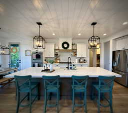 Kitchen with stainless steel refrigerator with ice dispenser, a chandelier, a sink, white cabinetry, and light stone countertops