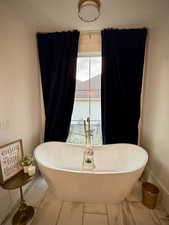 Full bathroom featuring marble look tile flooring, a freestanding bath, and baseboards