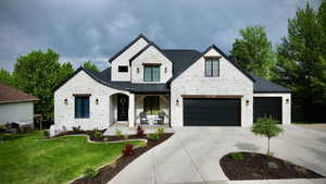 View of front of property featuring a porch, stone siding, a front lawn, driveway, and stucco siding