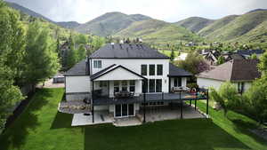 Rear view of house with a patio area, a deck with mountain view, a lawn, a shingled roof, and stucco siding