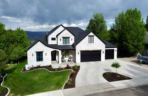 View of front facade with a porch, stone siding, driveway, a front lawn, and a garage