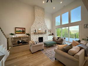 Living room featuring a towering ceiling, light wood-style flooring, a stone fireplace, stairway, and recessed lighting