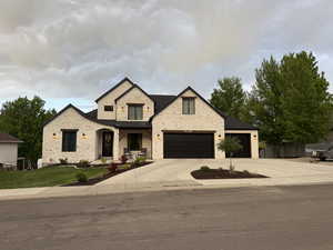View of front of house with stone siding, driveway, an attached garage, and a front yard