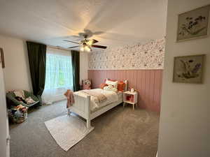 Bedroom featuring wainscoting, a textured ceiling, wallpapered walls, carpet floors, and a ceiling fan